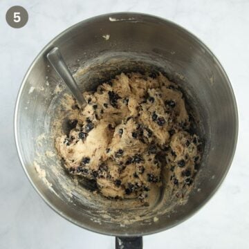 adding black currants to cake batter in a bowl using a spoon.