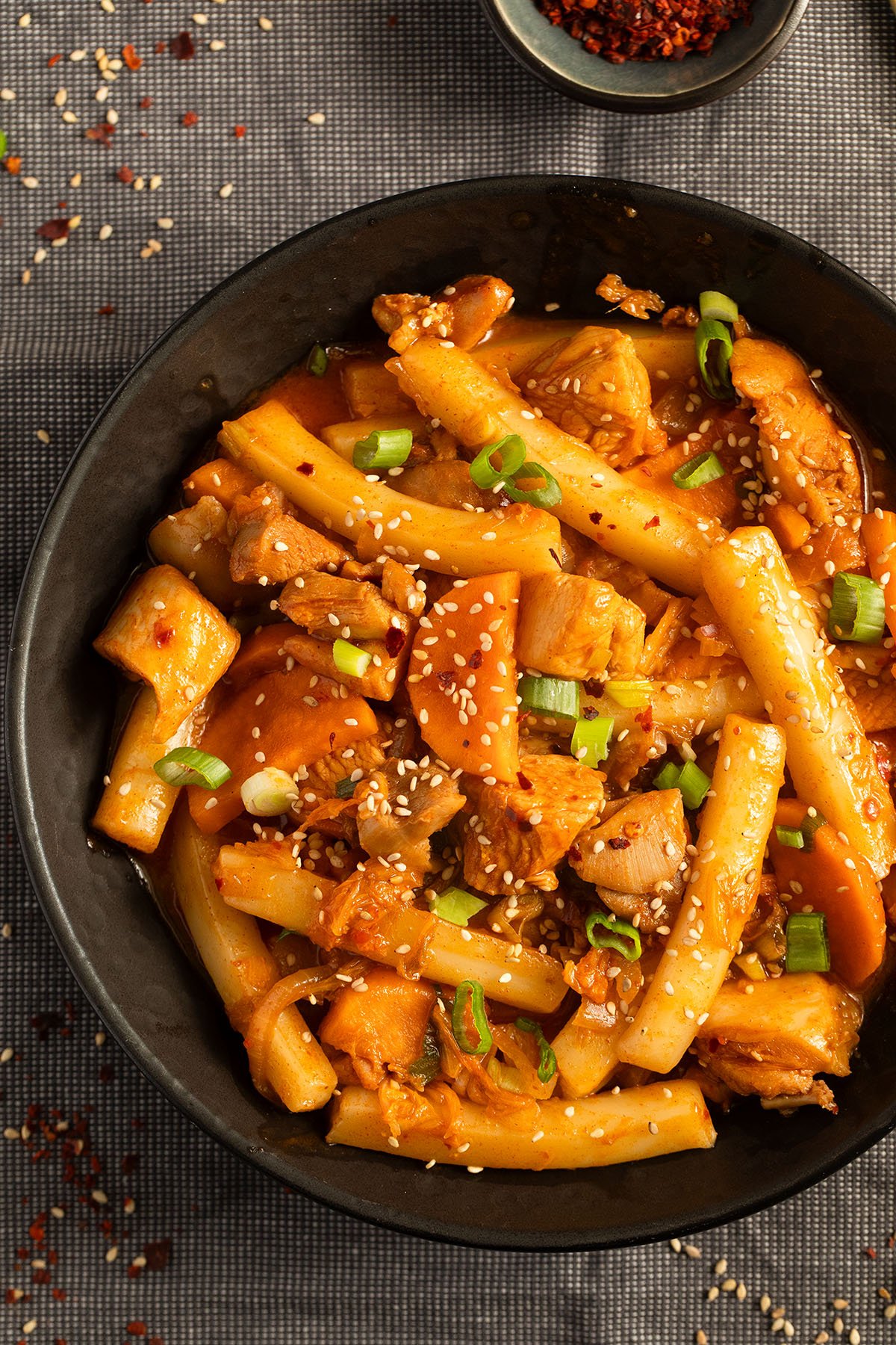rice cakes and chicken sprinkled with green onions and sesame seeds in a bowl.