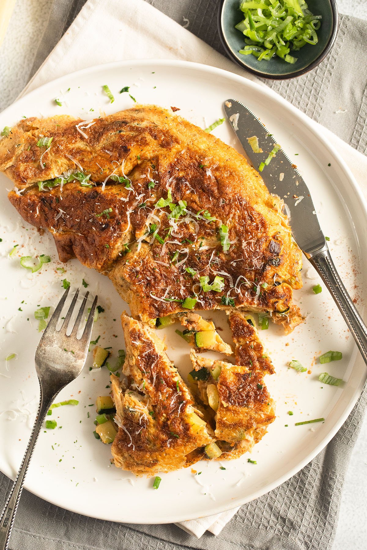 sliced zucchini omelette sprinkled with herbs on a plate with a fork and a knife.