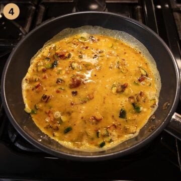 cooking omelette with zucchini in a small pan.