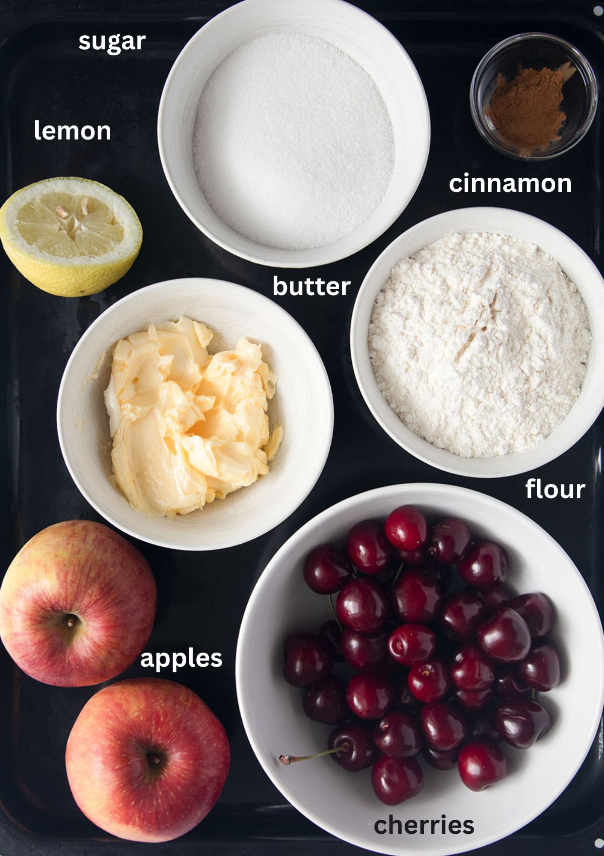 labeled ingredients for making cherry and apple crumble with butter, sugar, flour, cinnamon, and lemon.