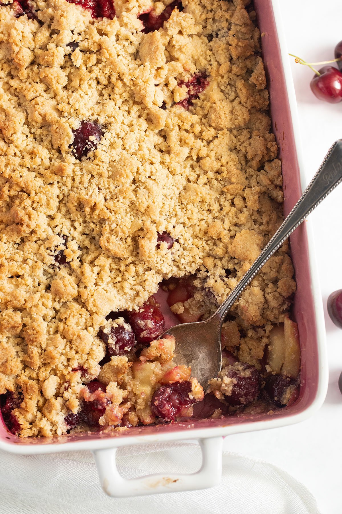 spooning cherry apple crumble from a golden brown bake.