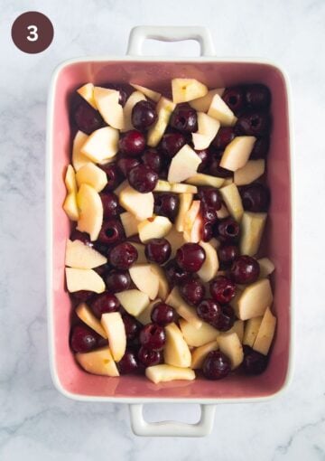 sliced apples and pitted cherries mixed in a baking dish to make crumble.