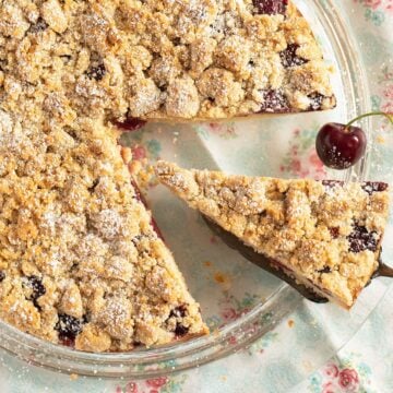 cherry crumble cake with a slice cut out of it.