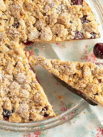 cherry crumble cake with a slice cut out of it.