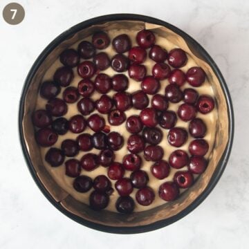 cake batter covered with fresh pitted cherries in a cake pan before baking.