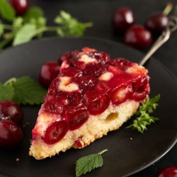 slice cherry upside down cake on a cake lifter with cherries and mint around it.