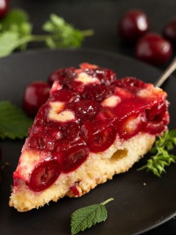 slice cherry upside down cake on a cake lifter with cherries and mint around it.
