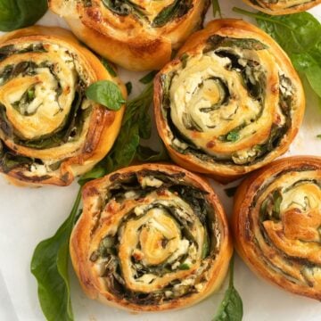 golden brown baked feta spinach rolls and spinach leaves around them.