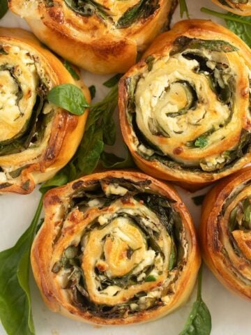 golden brown baked feta spinach rolls and spinach leaves around them.