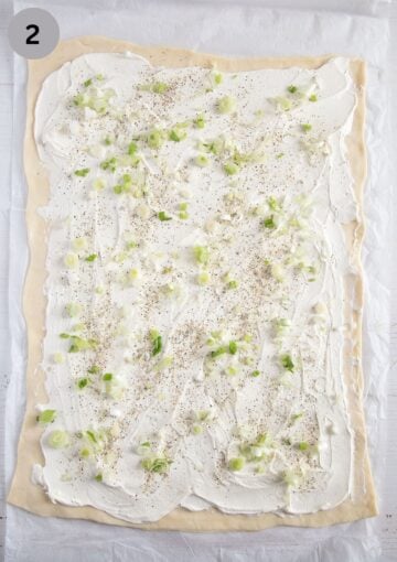 pizza dough spread with cream cheese and sprinkled with seasoning and sliced green onions.