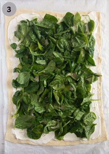 baby spinach spread on top of a rectangular piece of pizza dough for making rolls.