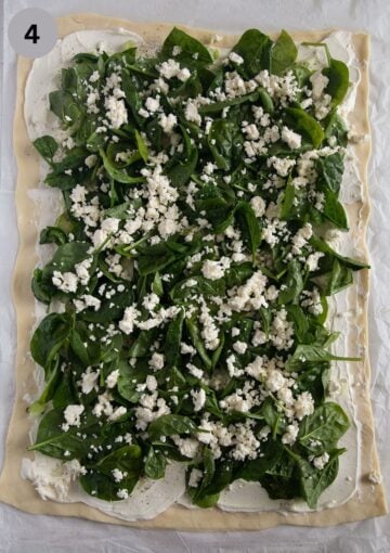 pizza dough spread with spinach leaves and feta for making rolls.