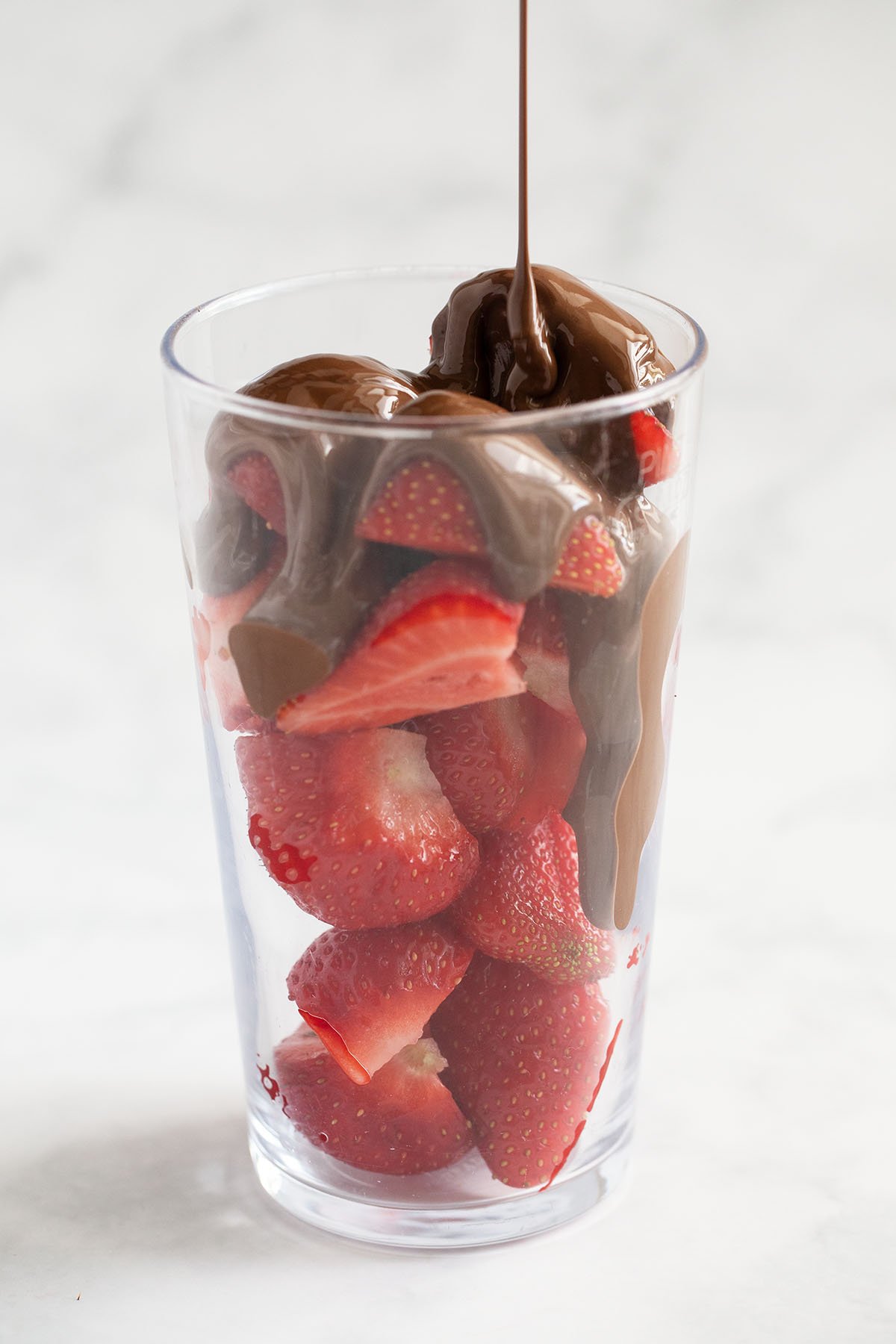 pouring melted milk chocolate over chopped strawberries in a glass.