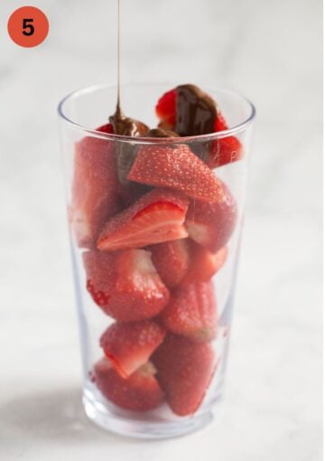 pouring melted chocolate in a thin stream over strawberries in a tall glass.