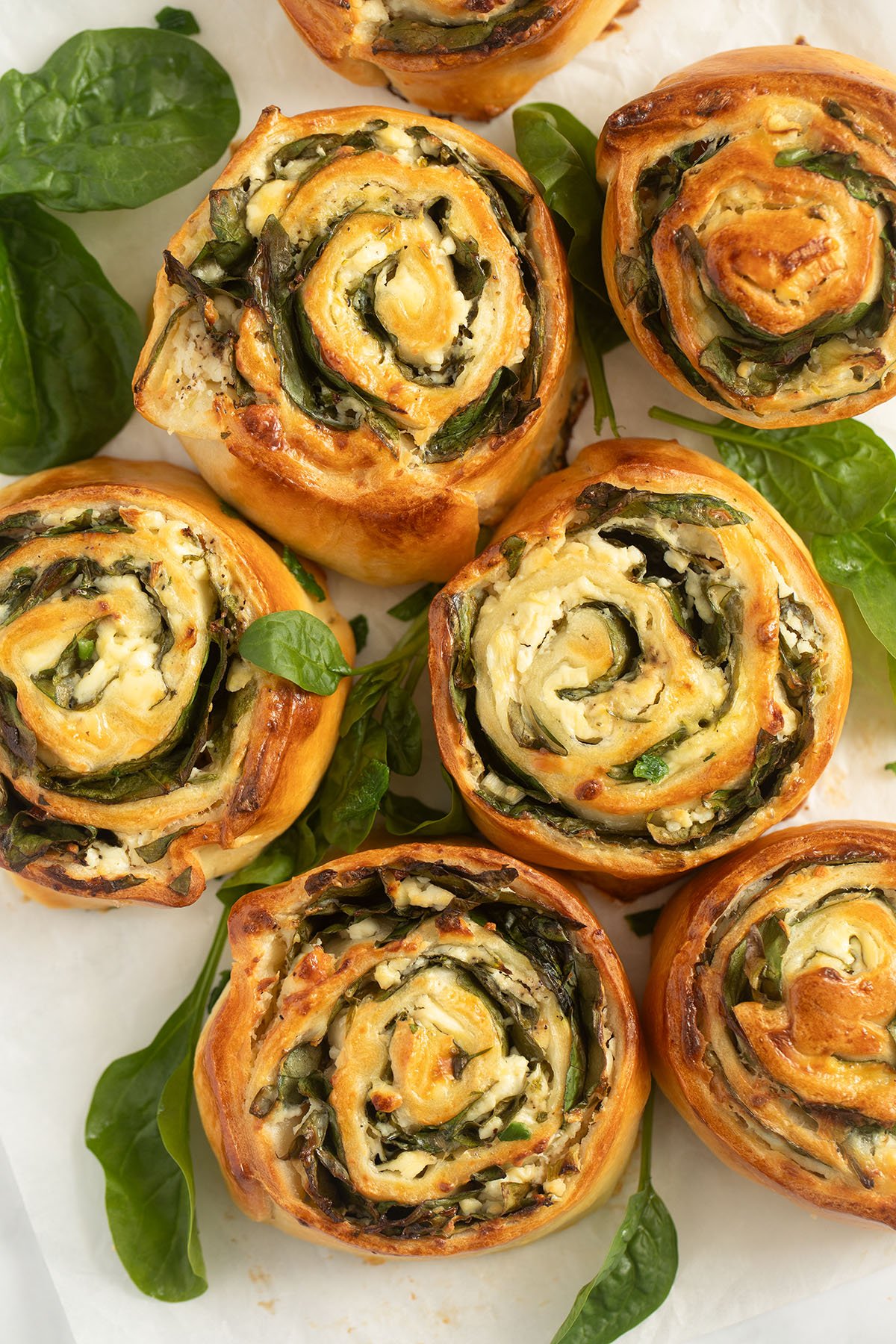 feta spinach rolls and spinach rolls on a white piece of parchment paper.