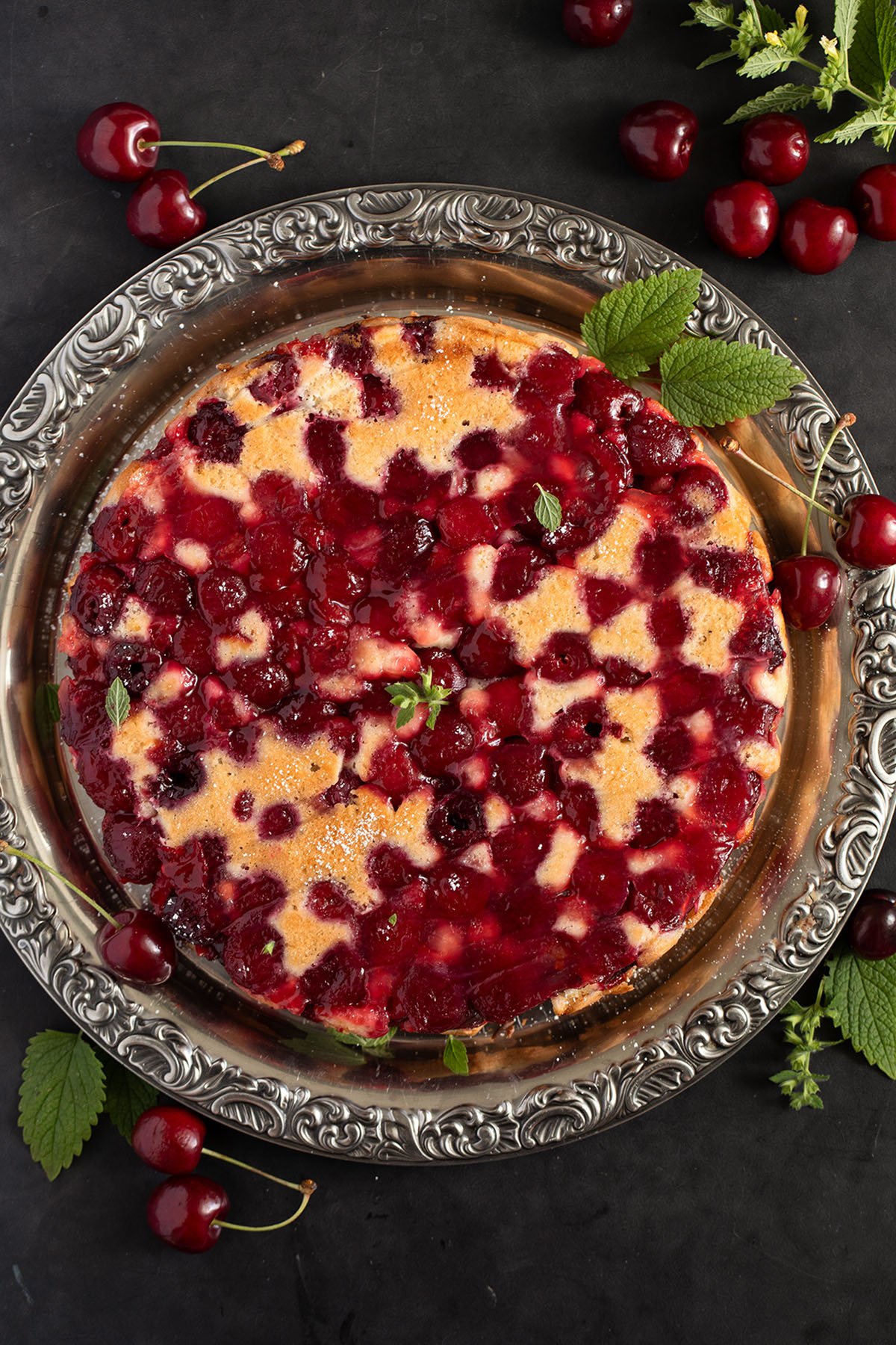 upside down baked cake with a cherry layer on top, many fresh cherries around it.