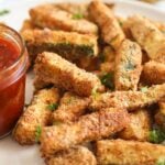 air fryer zucchini fries piled on a plate and served with red chili dip.