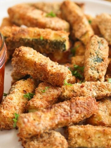 air fryer zucchini fries piled on a plate and served with red chili dip.