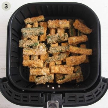 breaded zucchini fries stacked in the air fryer basket only halfway cooked.