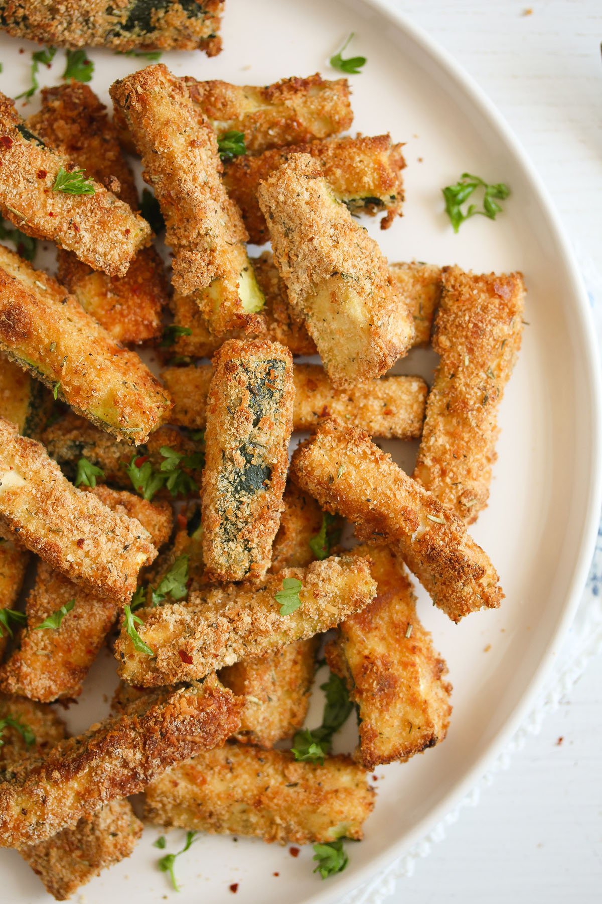 breaded air fryer zucchini fries sprinkled with parsley on a plate.