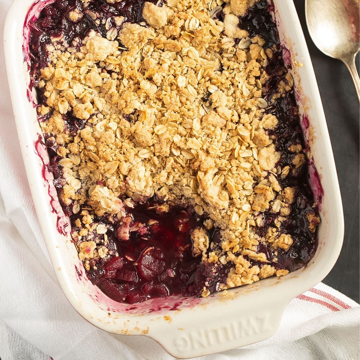 Golden apple and blueberry crumble with oat topping in a rustic baking dish.