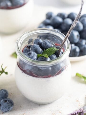 blueberry panna cotta in a jar and a bowl of fresh blueberries behind.