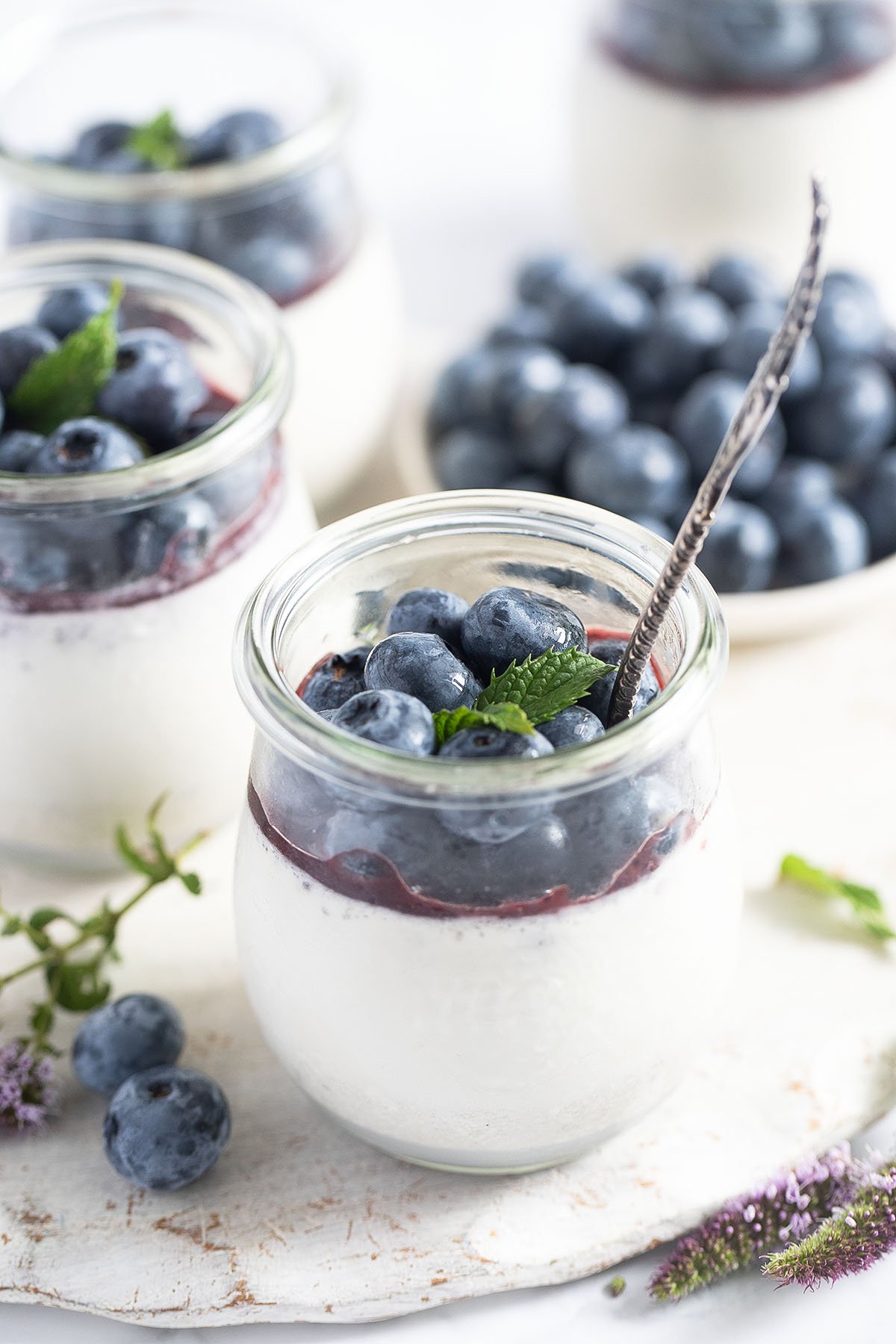 panna cotta topped with blueberry sauce and fresh blueberries in dessert jars, a bowl of berries in the back.