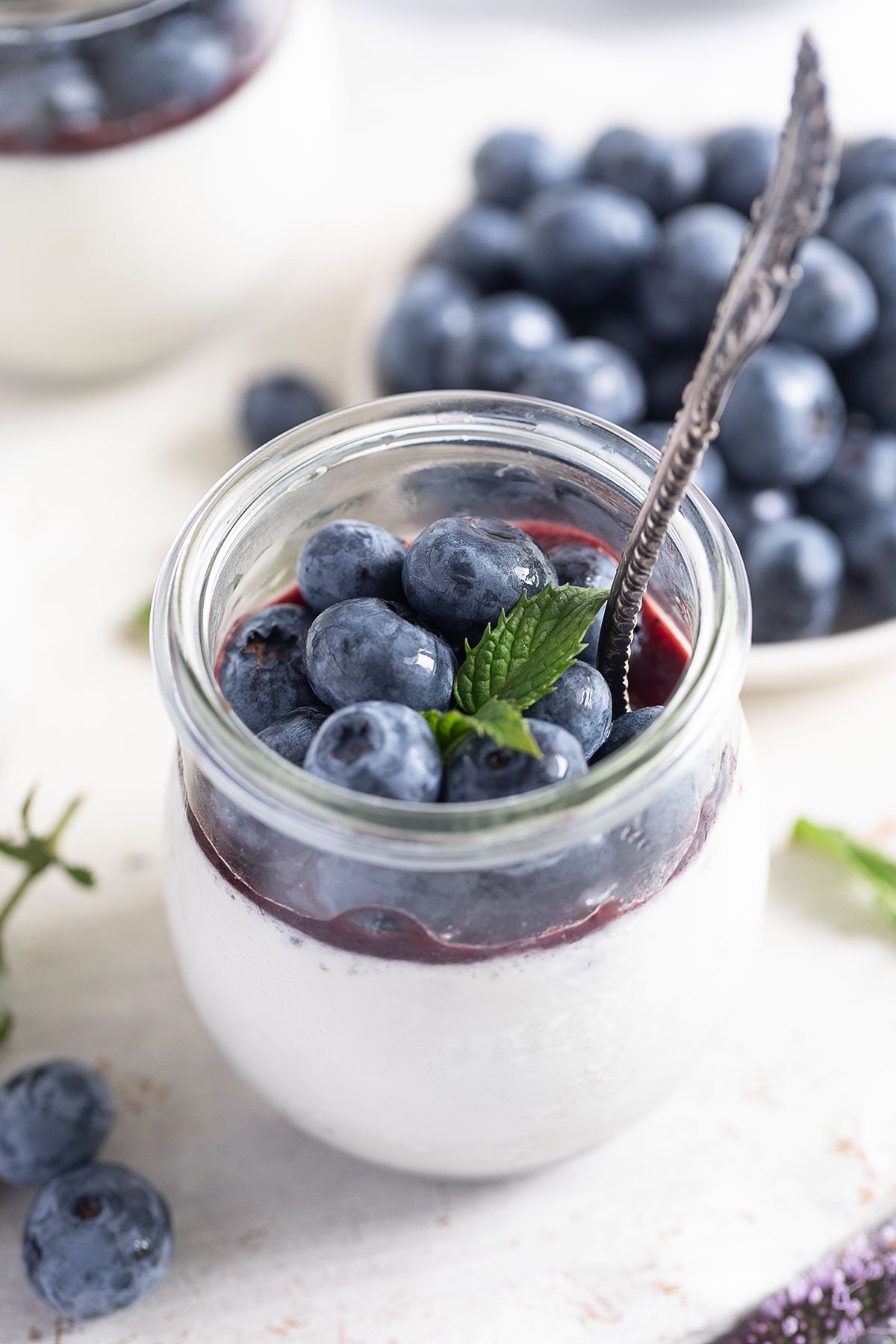 a dessert jar with panna cotta with blueberries with a spoon in it.