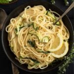 tangled goat cheese pasta with zucchini strips and lemon slices in a bowl.