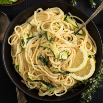 tangled goat cheese pasta with zucchini strips and lemon slices in a bowl.
