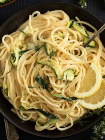 tangled goat cheese pasta with zucchini strips and lemon slices in a bowl.