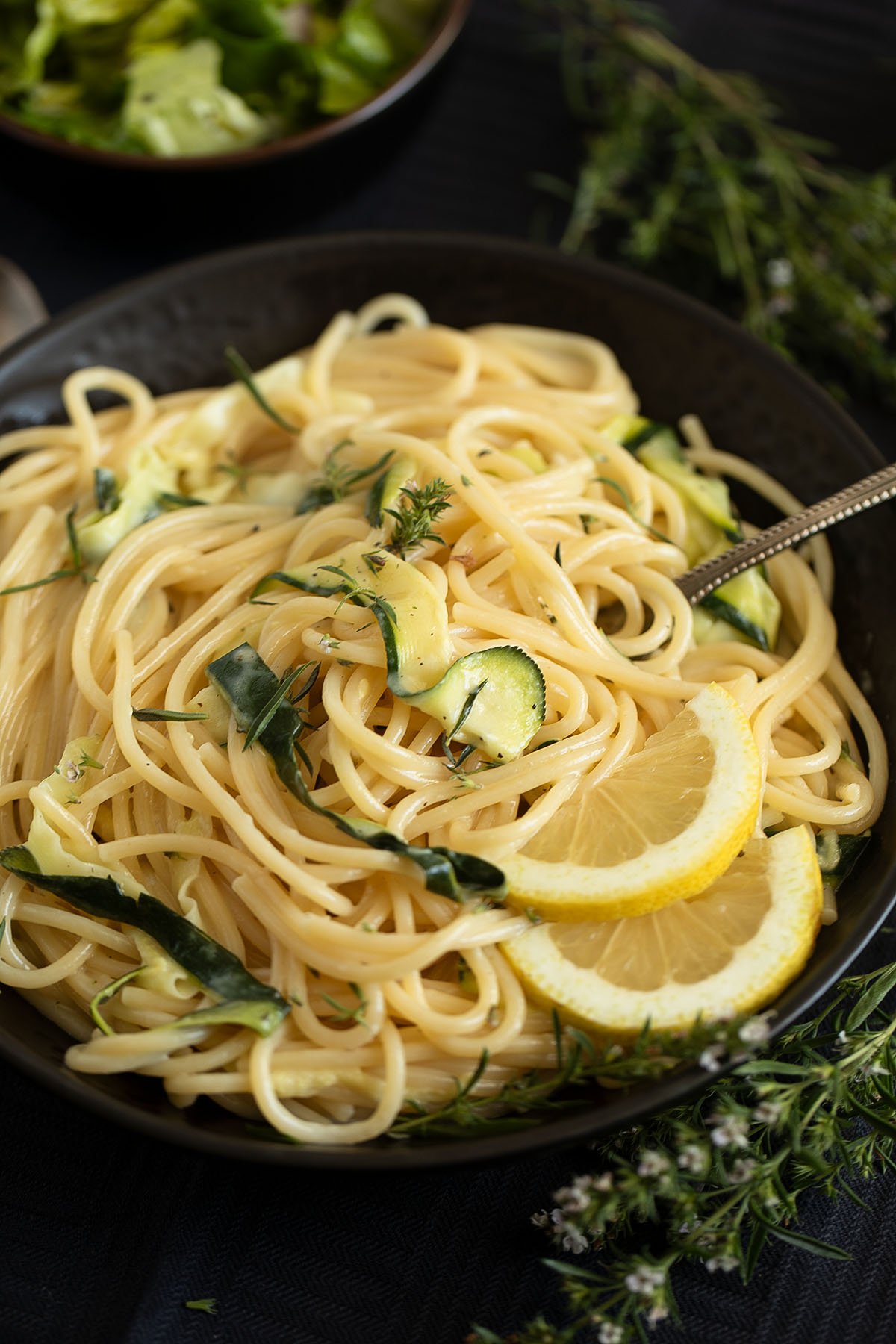 pasta with goat cheese and zucchini in a dark bowl, a bowl of salad on the side.