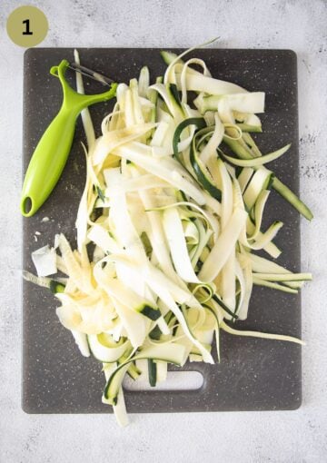 zucchini strips made with a vegetable peeler on a cutting board.