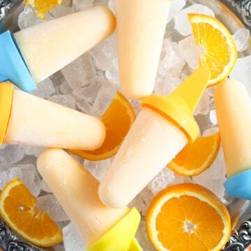 many orange popsicles and orange slices on ice cubes.