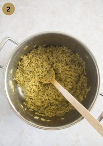 mixing coooked orzo with pesto in a large pot with a wooden spoon.