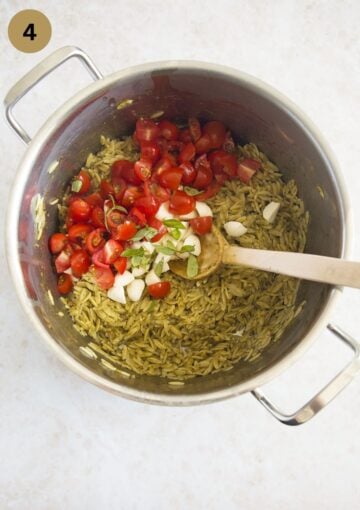 stirring cooked orzo, pesto, tomatoes, mozzarella, and basil in a pot with a wooden spoon.