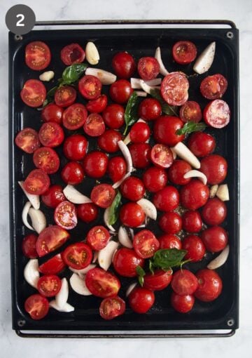 chopped tomatoes, sliced onions and garlic cloves on a baking sheet before baking.