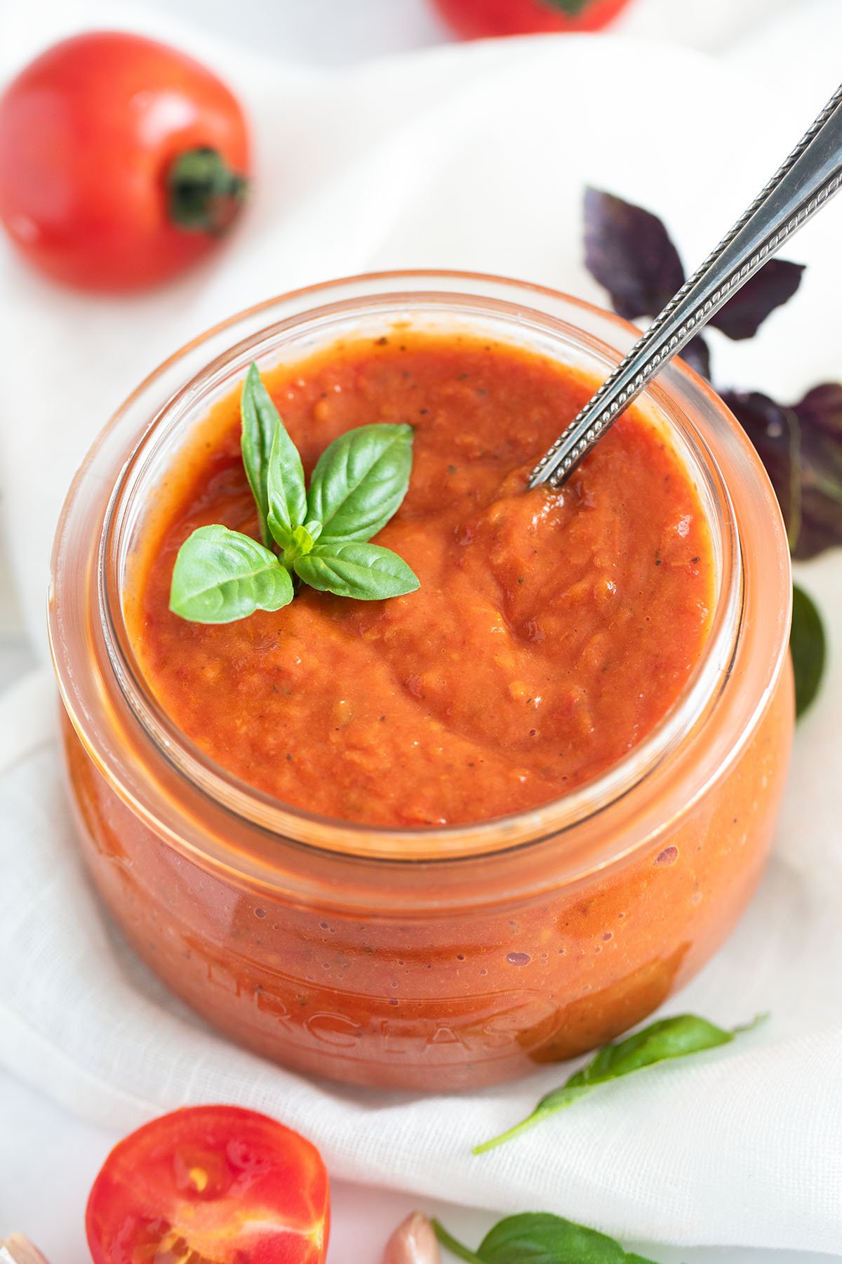 roasted tomato pasta sauce in a large bowl, some tomatoes, and basil leaves around it.