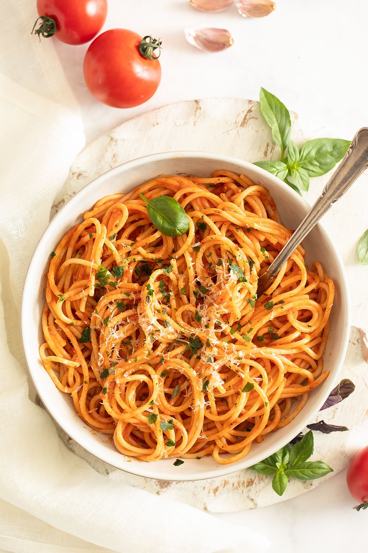 a plate full of pasta with roasted tomato sauce, two small tomatoes and basil leaves around it.