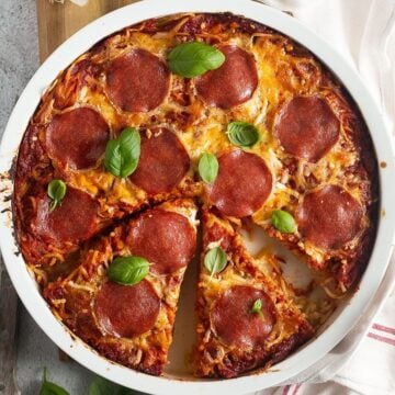 Golden baked spaghetti pizza with melted cheese and salami slices, served in a round ceramic dish.
