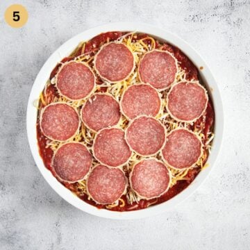 Spaghetti pizza topped with grated cheese and slices of salami, ready to be baked.