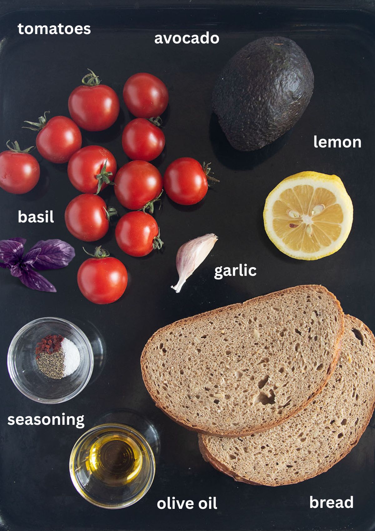 labeled ingredients for making toast with cherry tomatoes, avocado, lemon, btread, and basil.