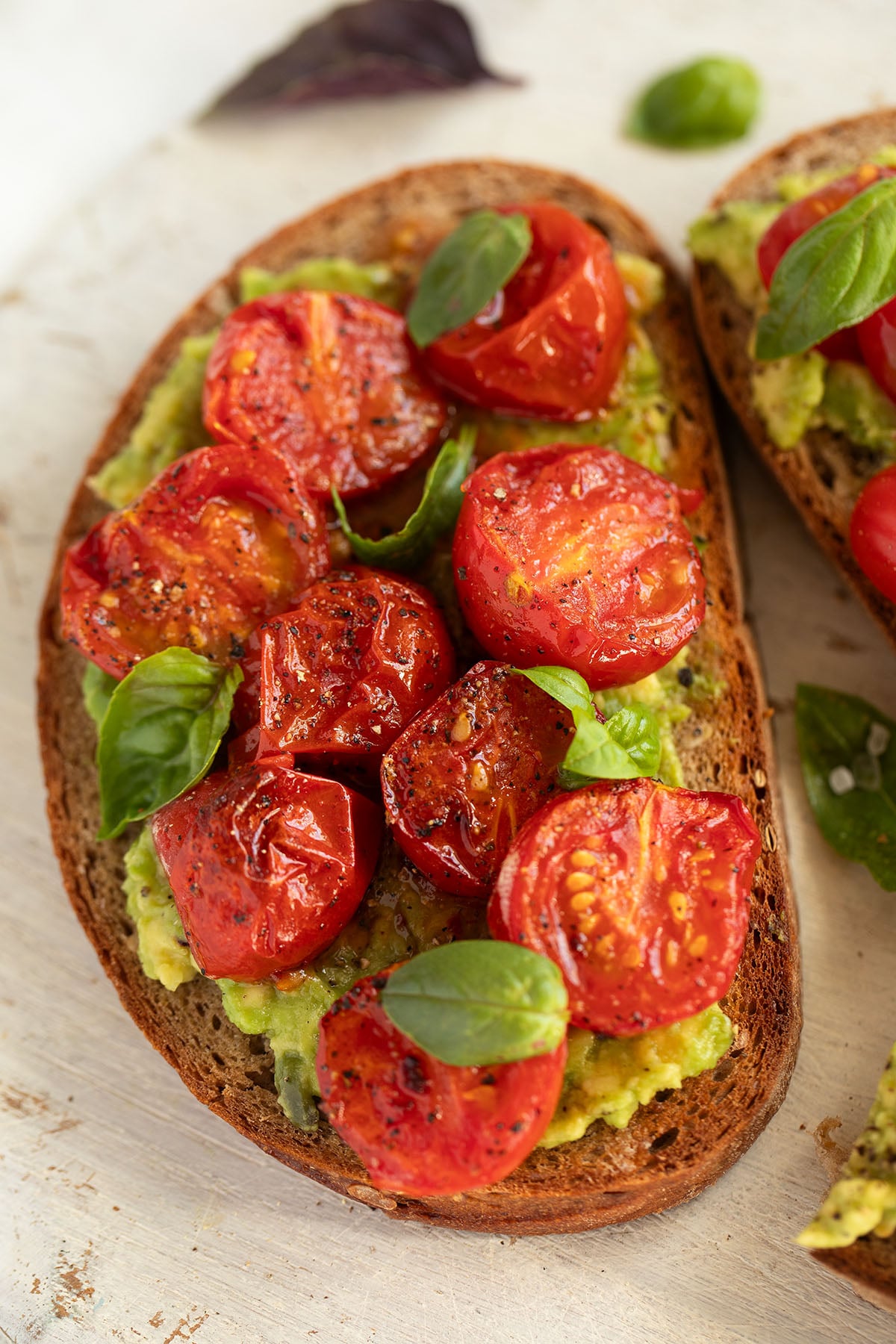 one large toast with roasted tomatoes and mashed avocado and basil leaves.