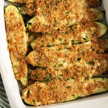 baked zucchini with feta topped with breadcrumbs and parsley in a baking dish.