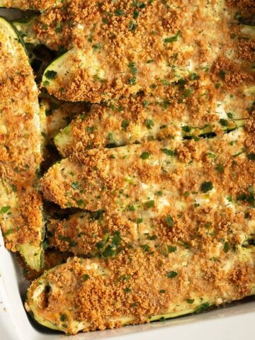 baked zucchini with feta topped with breadcrumbs and parsley in a baking dish.