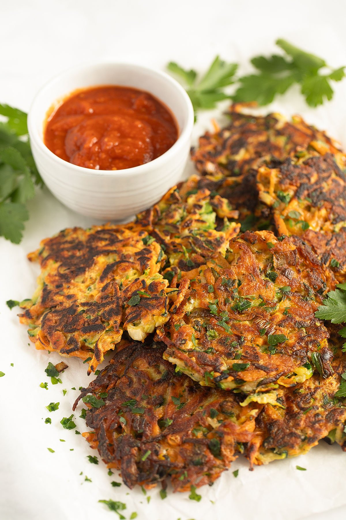 fritters with sweet potatoes and zucchini, a bowl of chili dip for serving and parsley leaves.