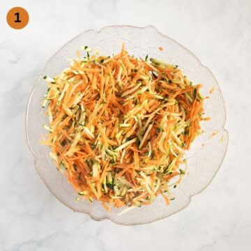 grated zucchini and sweet potatoes mixed with salt in a bowl.