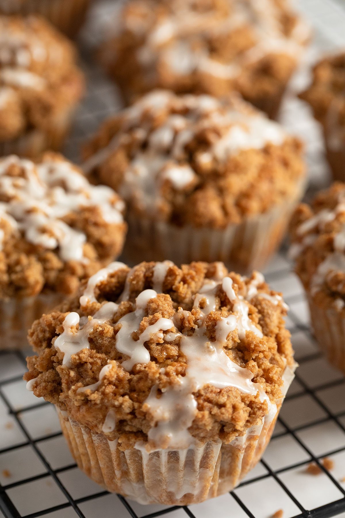 many apple muffins with crumbles and lemon glaze on a wire rack.