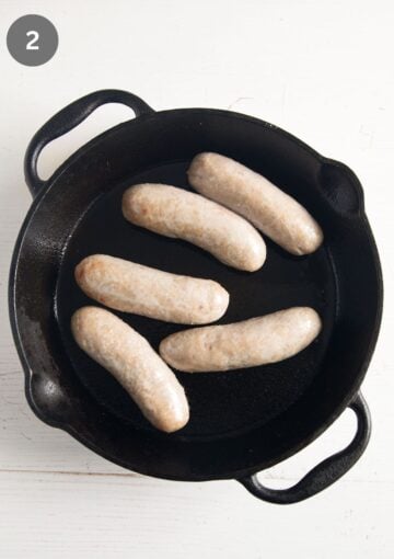 five sausages baked halfway through in a skillet.